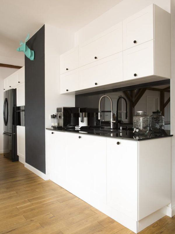 Side view of white kitchen interior with black countertop and wooden floor